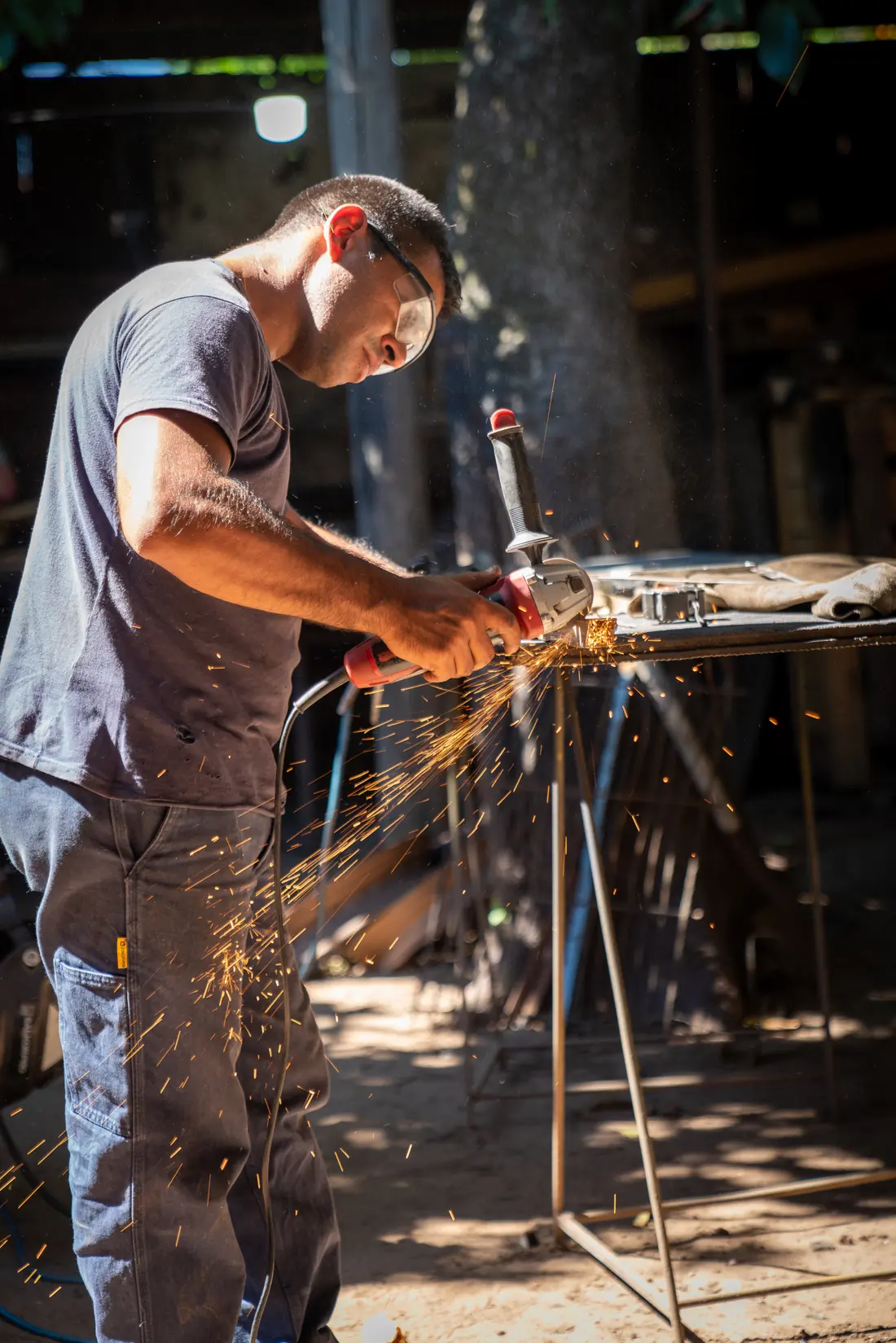 Métallier découpant à la meuleuse le profilé d’acier d’un portail en atelier de fabrication, dans une gerbe d’étincelles